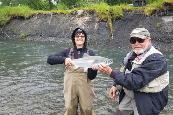 two people holding up a fish while standing in a river